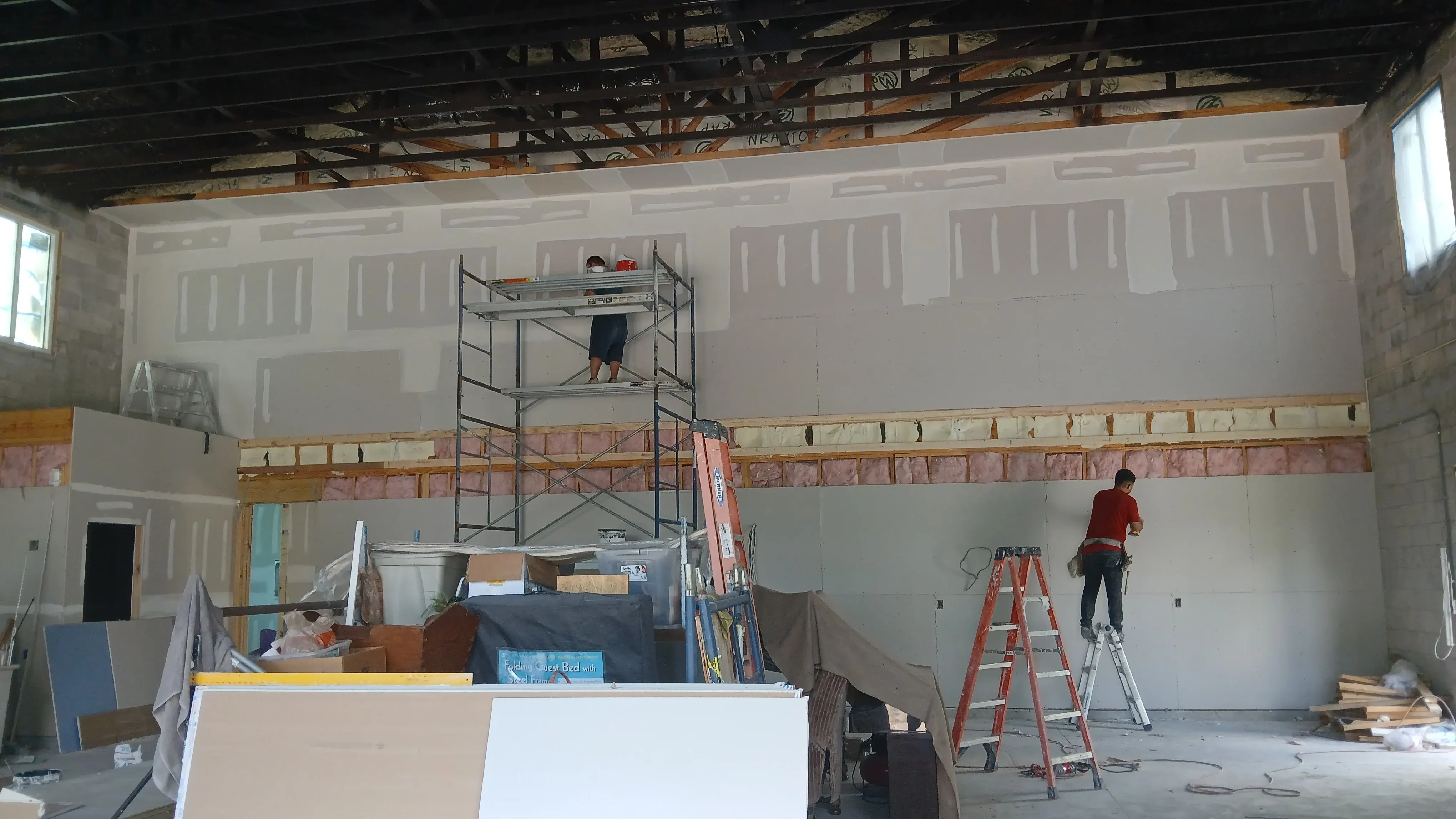 Drywall crew hanging board on a tall wall with scaffolding and ladders, drywall installation in Lehigh Acres